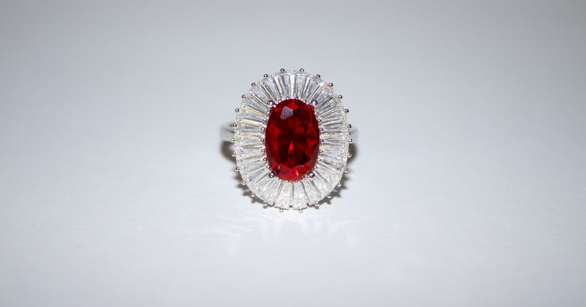 A faceted red ruby set in a diamond-halo ring on a grey surface