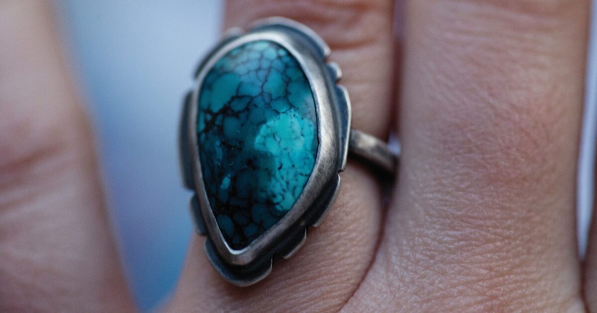 A silver ring set with a blue turquoise stone showing dark spiderweb matrix veining