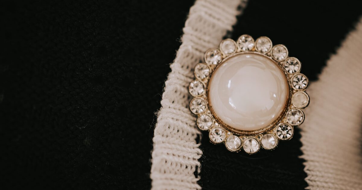 A vintage rhinestone and faux-pearl costume brooch pinned to a knit cardigan