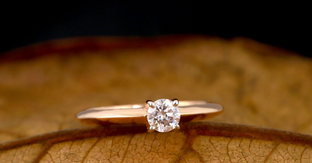A brilliant-cut solitaire diamond ring resting on a dry autumn leaf