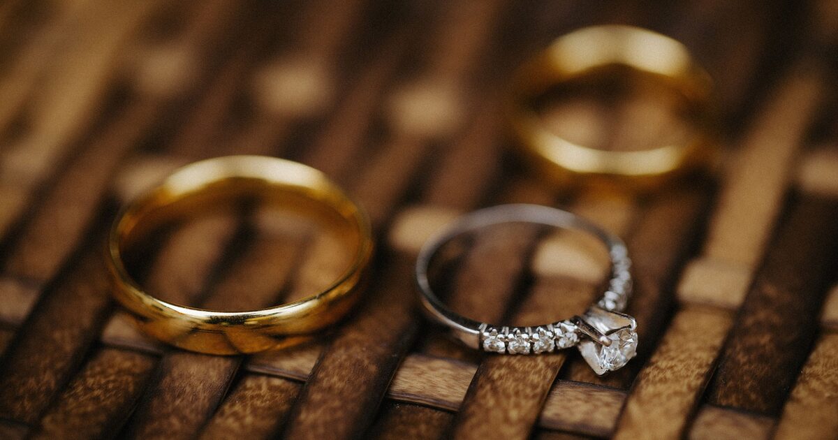Close-up of a gold wedding band beside a diamond ring on a wooden surface